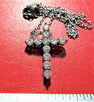 Silver-tone cross pendant with round clear cubic zirconia stones on matching chain placed on red background near inch ruler for size reference.