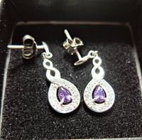 Pair of sterling silver earrings with teardrop amethyst stones on black velvet background.