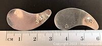 Top-down view of the earrings face down next to a ruler showing length between 5-6 cm, showing their abstract, curved shape and 925 sterling silver mark on the back.