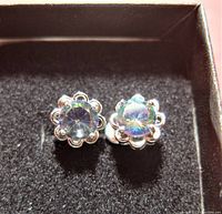 Close up view of pair of sterling silver stud earrings with round mystic topaz stones set in decorative floral bezels.
