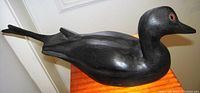 Side angle view of black wooden duck decoy showing split tail and smooth paint finish.