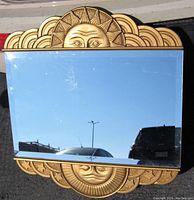 Front view of mirror showing gold-tone carved sun motif at top and beveled glass surface