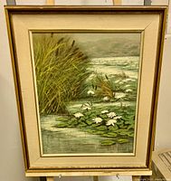 Frontal view of the framed oil painting showing the water lilies and reeds in nature.