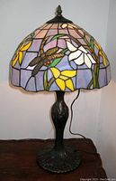 Full view of the lamp showing the stained glass shade with dragonfly and floral motif and dark metal base.