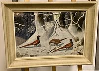 Full view of the framed oil painting showing the three pheasants in a snowy forest landscape with artist signature visible.