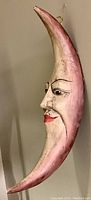 Side angled view showing the crescent moon shape with carved man face and painted in natural wood and red tones.