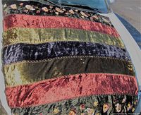 Top down photo showing the entire throw blanket laid flat on a white car hood with visible alternating satin velvet stripes in various colors and embroidered floral panels on either side.