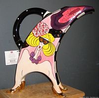 Side view showing overall colorful painted female figure, gold shoes, black handle, floral hat, and purple necklace.