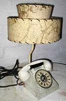Mid-century modern table lamp shaped like a vintage telephone, showing cream and brown streaked double-decker fabric lampshade, metal base, rotary dial with Roman numerals, and attached handset.