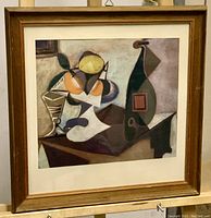 Framed Picasso art print in wooden frame showing abstract cubist still life with oranges, lemons, bottle, and glass.