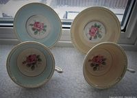 Top view showing the interiors of two tea cups and their matching saucers featuring pink cabbage rose on blue and beige backgrounds.