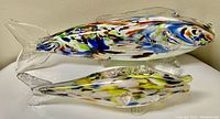 Side view showing both fish sculptures with colorful designs and clear glass fins and tails.