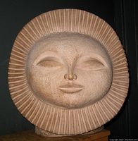 Front angled view of terracotta sun face sculpture showing detailed facial features and ridged halo.