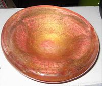 Top angle view showing golden bullicante pattern swirled inside clear glass bowl with reddish undertones.