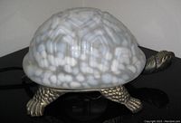 Side view of the tortoise table lamp showing the white and gray patterned glass shell and metal tortoise body and feet.