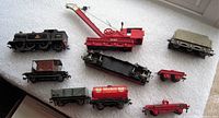 Overview of all nine pieces in the Hornby Dublo train set arranged on a white fabric surface, showing locomotive, crane, and various cars.