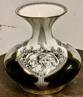 Front and angled views of a porcelain vase with black base color and white faces in Art Nouveau style, trimmed with gold on the rim