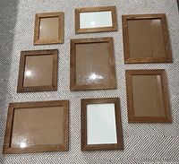 Seven natural wood framed glass picture frames arranged on patterned fabric surface. Sizes vary from approx 10.5x13 to 15.5x18.5 inches.