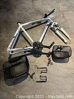 White Raleigh bike frame with front fork and crankset with two pedal arms visible, assorted bicycle parts including wire baskets and water bottle cages around it