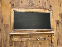 Front view of wooden chalkboard with black writing surface and five coat hooks beneath.