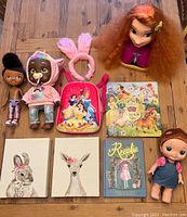 Photo of children's toys, dolls, books, canvas wall art, and accessories laid out on wooden table