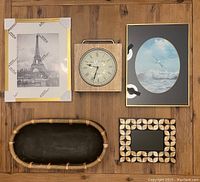 Front view of lot showing five items including gold frame with Eiffel Tower art, ocean scene frame, square clock, decorative oval wood tray, and small leaf-pattern frame.