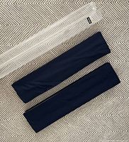 Photo showing two folded navy blue cordless Roman cellular shades without hardware, laying on carpet. One clear protective plastic sleeve on top.