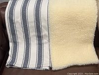Photo showing the side-by-side view of the blue and white striped cotton throw and the beige fluffy throw or rug, highlighting textures and colors.