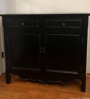 Front view of black entryway cabinet showing two drawers with metal knobs and two doors with metal handles, with curved bottom edge detail.