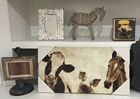 Shelf display showing farmhouse canvas featuring cow, pig, and horse illustration, white decorative frame, metal horse silhouette, Kirkland wooden frame without glass, and a small decorative box with pig design.