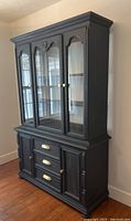 Front view of entire gray two-piece china cabinet with gold hardware, showing bottom drawers and doors and upper glass doors