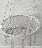 Front view of white woven rope hammock chair showing rope lattice seat, circular frame and tassel fringe.