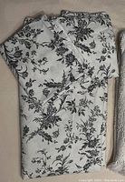 Folded white duvet cover and pillowcases with black floral pattern on a beige surface