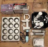Full lot overview: jumbo muffin pan, KitchenAid food grinder attachment with cones, rotor shredder/slicer attachment, storage box with additional KitchenAid parts and attachments, some parts in original boxes