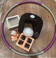 Top down view of all items arranged on wooden table showing hula hoop, neck massager, stones, diffuser, and book.