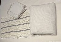 Queen white cotton duvet cover and pillowcases folded, alongside two striped pom-pom throw pillow covers.