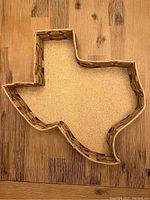 Top view of wicker and rattan tray shaped like Texas with cork bottom on wooden surface.