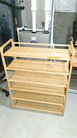 Front view of one bamboo shoe rack with four slatted shelves in a basement area, showing open design and light bamboo color.