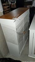 Side and front angled view of the painted cabinet showing the white painted body with vertical grooves on doors and natural wood finished top.