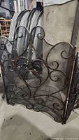 Front angled view of the wrought iron fireplace screen showing decorative swirl pattern and mesh backing.