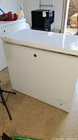 Front and side view of the white chest freezer showing dents and scratches on the body and lid.