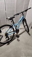 Full rear and side view of light blue Jamis mountain bike with knobby tires and black handlebar in basement area