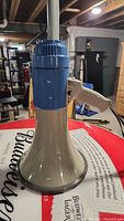 Front view of the megaphone showing beige horn and blue electronic top with a beige handle.