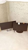 Two monitors placed side by side on a floor against a wall, showing both screens and stands.