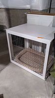 Pet crate front view showing white painted wood frame with black metal bars and cushioned pet bed inside.