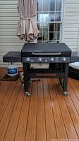 Front view of the closed-lid grill on a wooden deck, showing frame, wheels, and side shelf
