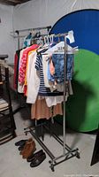 Photo showing one of the garment racks with clothing hanging on it and shoes on the floor below.