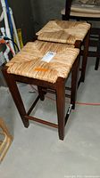 Two wooden stools with rush woven seats placed on a concrete floor in a basement setting.