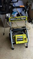 Full view of Ryobi pressure washer showing the frame, handle, wires, and front label indicating 2000 PSI and 1.2 GPM.