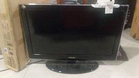 Front view of the Samsung flat-screen TV showing screen and stand with tape on the frame corners.